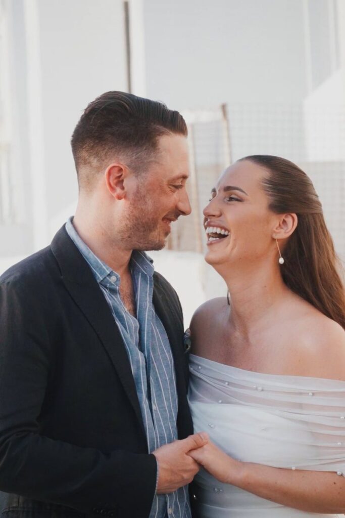 Evelin and Luke laughing together by the sea on Paros during their four-day wedding, filmed by Konstantinos Liopetas