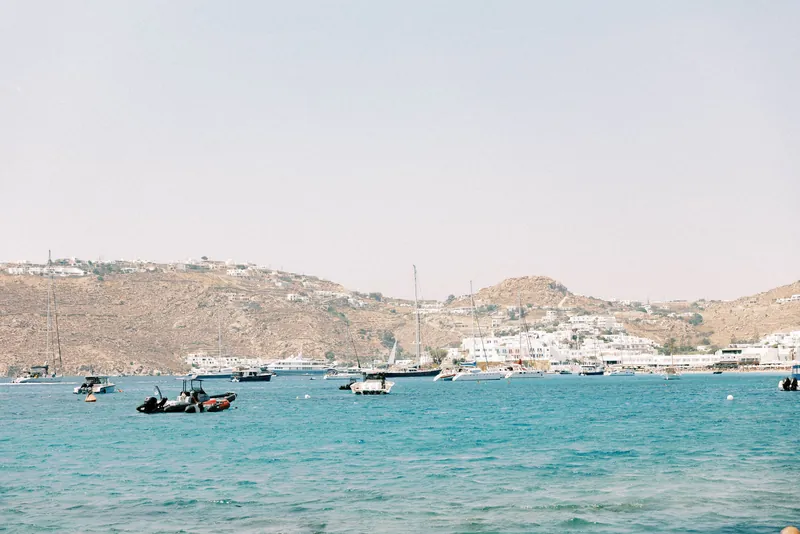 Sailing boats moored in a turquoise bay below the whitewashed hills of Mykonos